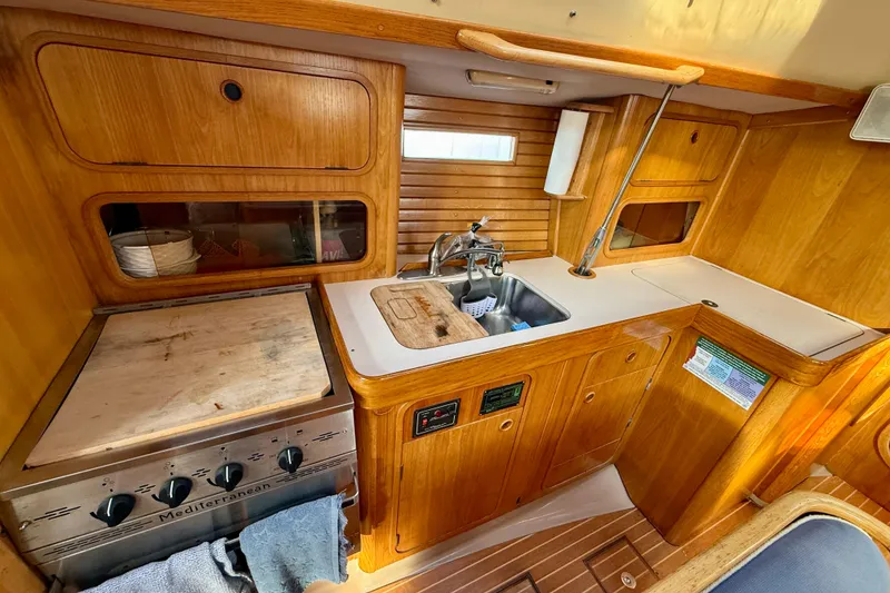 Interior view of 1988 Beneteau Oceanis 390 yacht kitchen with wooden cabinetry and stove.