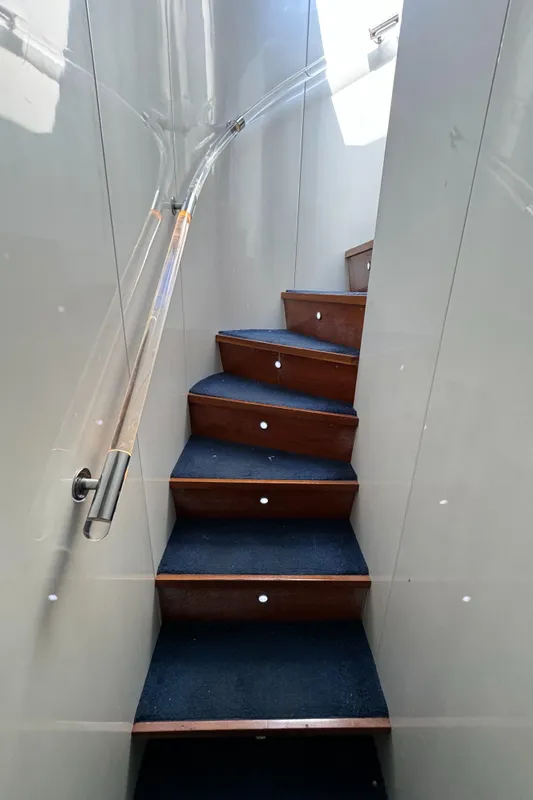 Staircase inside 1990 Versilcraft Challenger Motor Yacht with blue carpet and wooden steps.