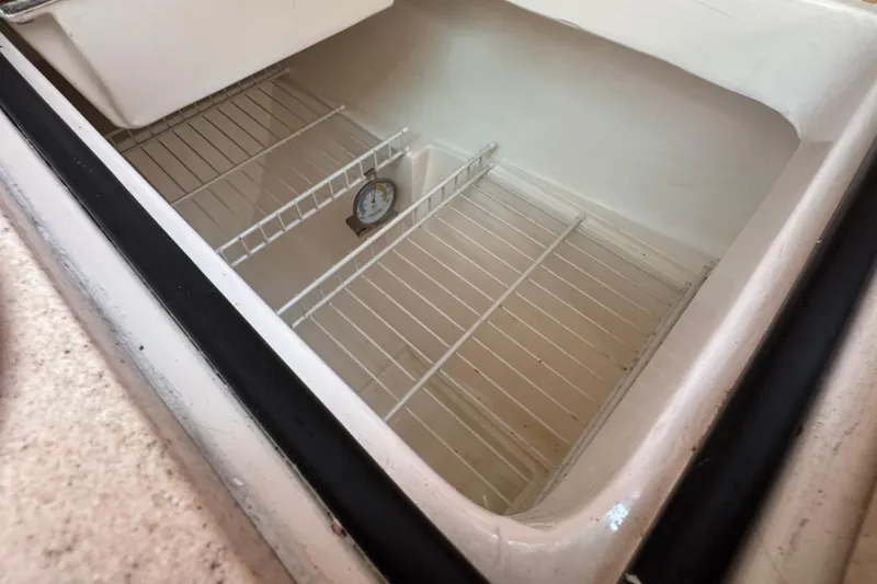 Empty refrigerator compartment in a 1997 Catalina 36 MkII boat, featuring wire shelves and a thermometer.