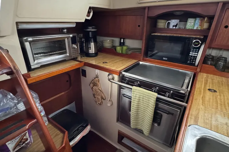 Compact kitchen in 1985 Catalina 36 MK1 sailboat with appliances and wooden cabinetry.