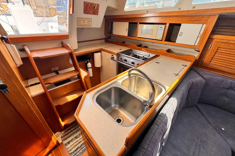 Interior of a 1995 Catalina 36 MkII sailboat kitchen with sink, stove, and seating area.