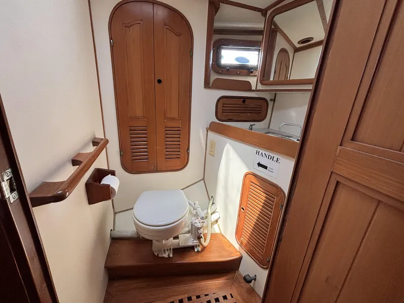 Wood-paneled bathroom in 1982 Norseman 447 yacht, featuring toilet, sink, and storage cabinets.