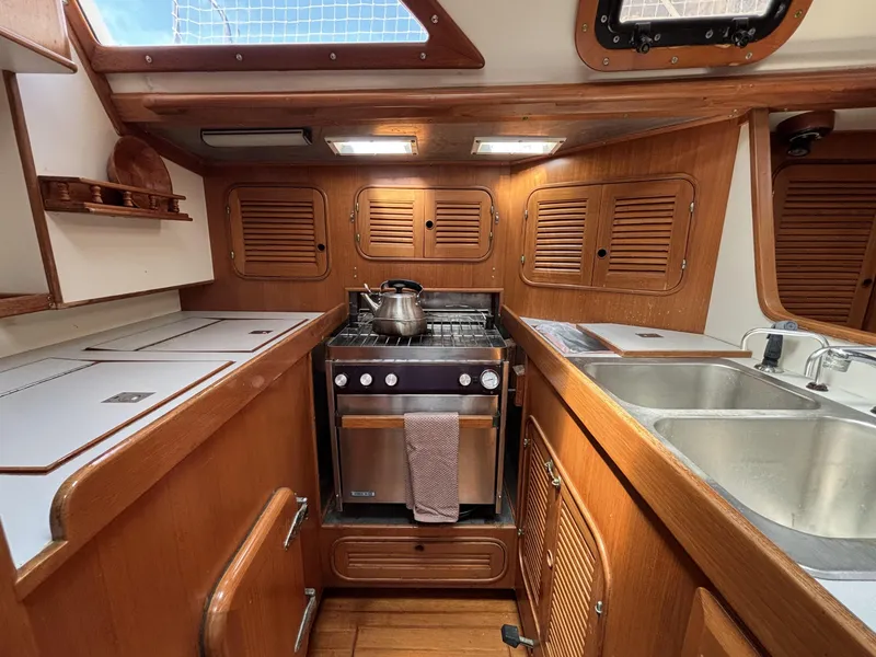 1982 Norseman 447 yacht kitchen with wooden cabinets, stove, and stainless steel sink.
