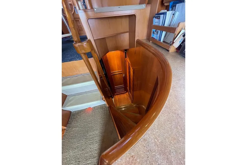 Staircase inside 1990 Offshore Yachts 55 Pilothouse, featuring wooden interior and bookshelves.