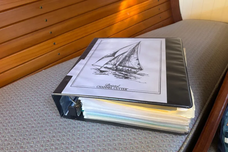 Binder with Bristol Channel Cutter 28 sailboat documents, 1983, on a wooden bench.