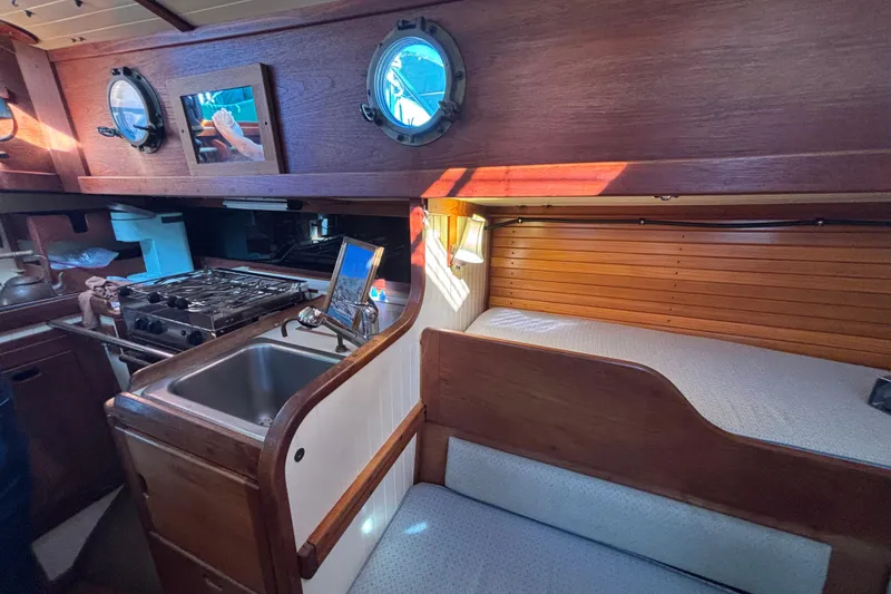 1983 Bristol Channel Cutter 28 interior with wooden cabinetry, sink, stove, and cozy seating area.