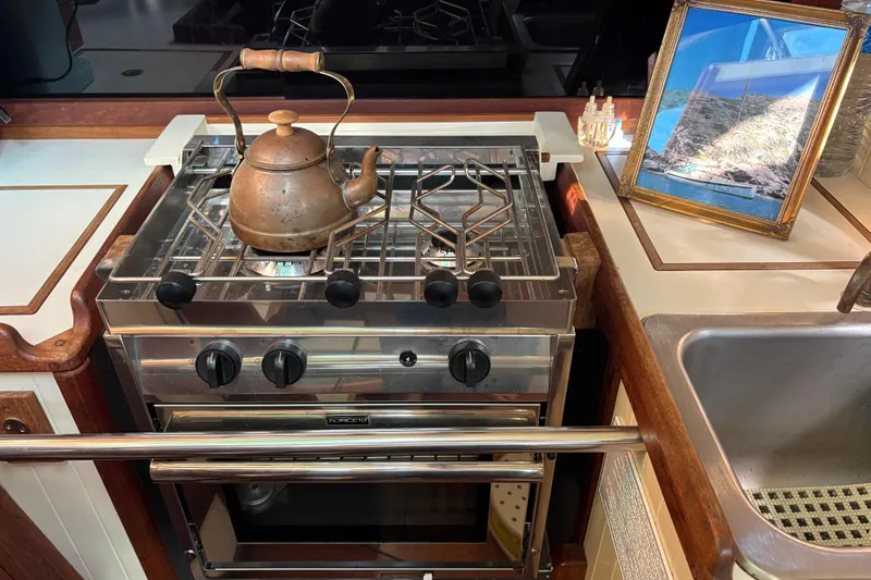 Galley kitchen in 1983 Bristol Channel Cutter 28 with stove, kettle, and framed photo.