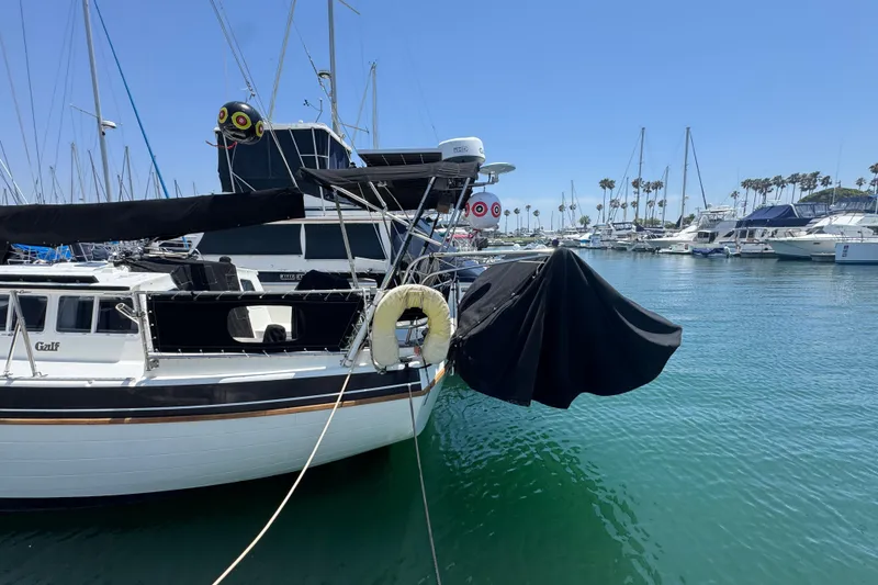 1989 Gulf Pilot House yacht docked in a marina, surrounded by sailboats and clear blue water.