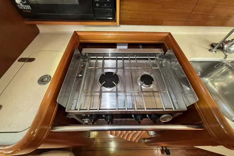 Two-burner stove in 1997 Beneteau Oceanis 400 yacht kitchen, with wooden cabinetry and sink.