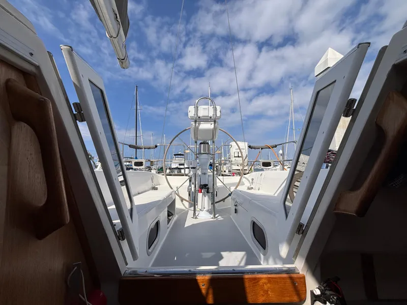 2005 Catalina 320 sailboat cockpit with steering wheel, docked under a blue sky with clouds.