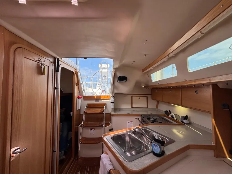 Interior of 2005 Catalina 320 sailboat, featuring a compact kitchen with wooden cabinetry and stainless steel sink.