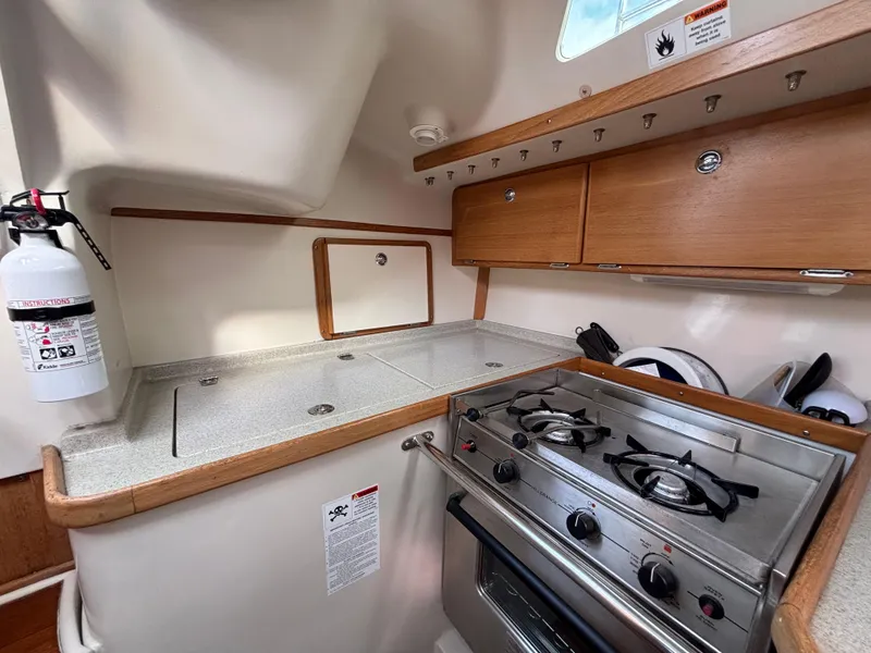 Compact kitchen in a 2005 Catalina 320 sailboat with stove, storage, and fire extinguisher.