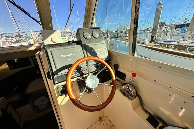 2003 Albin 28 TE boat helm with Raymarine navigation, wooden steering wheel, marina view.
