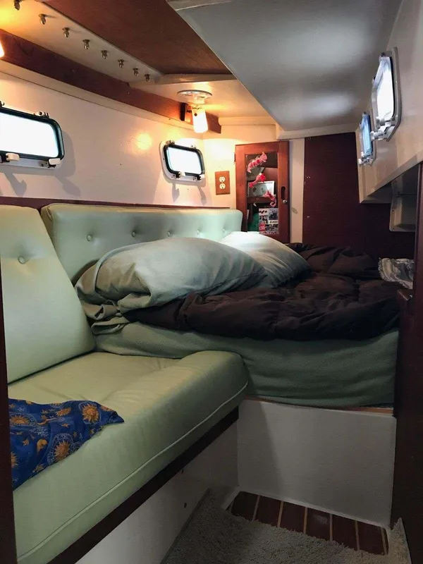 Cozy interior of 1986 Catalina 34 sailboat with cushioned seating and bedding.