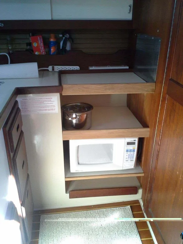 1986 Catalina 34 yacht kitchen with microwave, wooden shelves, and storage.