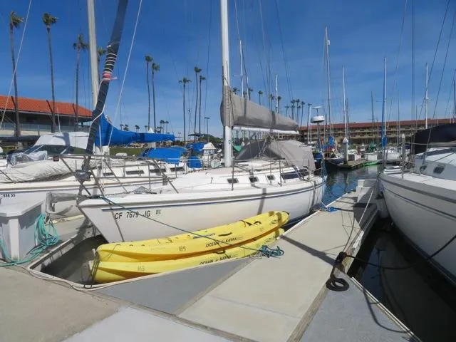 1986 Catalina 34 sailboat docked with yellow kayak, clear sky, and marina backdrop.
