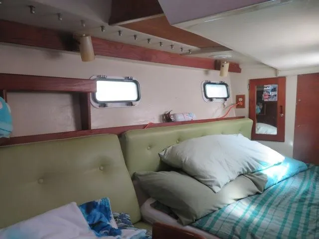 Cozy cabin interior of a 1986 Catalina 34 sailboat with green cushions and porthole windows.