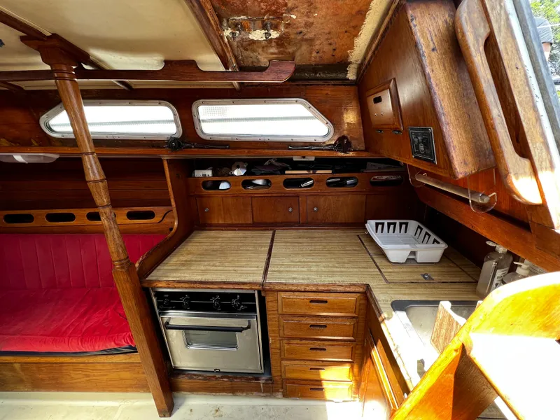 1978 Ericson 35 Sloop interior with wooden cabinetry, stove, and red seating.