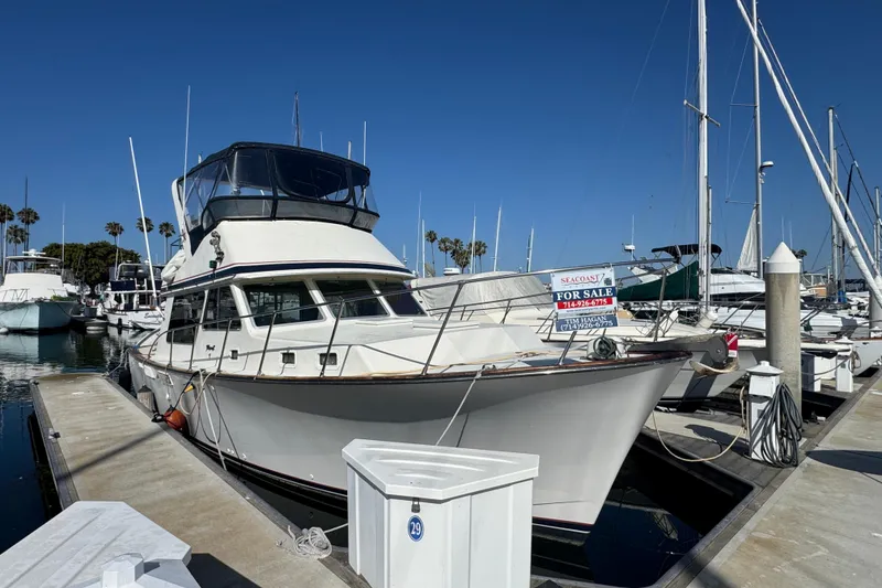 1977 Tollycraft 37 Convertible yacht docked, for sale sign visible, clear blue sky.