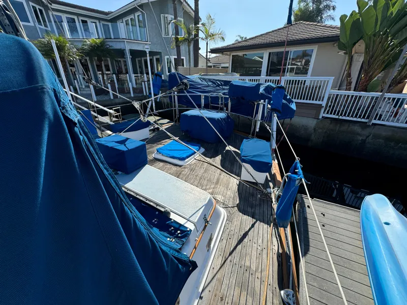 1984 Transpacific Marine Ketch docked, covered in blue tarps, near waterfront homes.