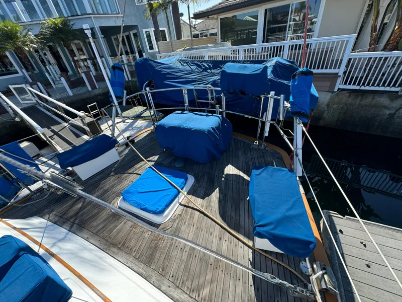 1984 Transpacific Marine Ketch with blue covers docked near waterfront homes.