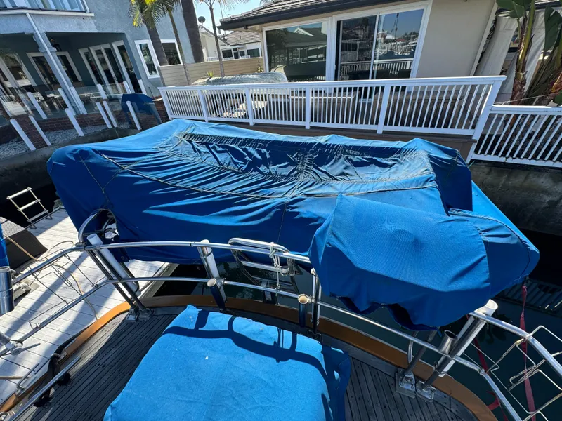 1984 Transpacific Marine Ketch with blue covers docked near waterfront homes.