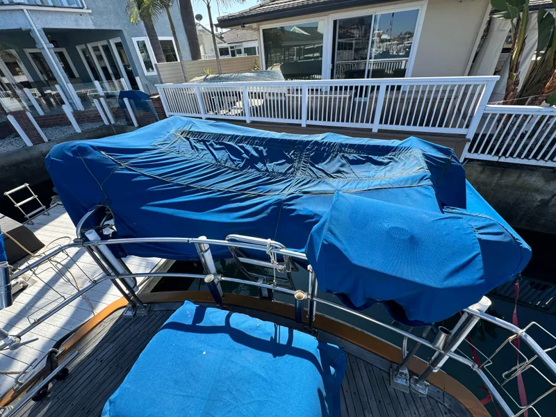 1984 Transpacific Marine Ketch with blue covers docked near waterfront homes.