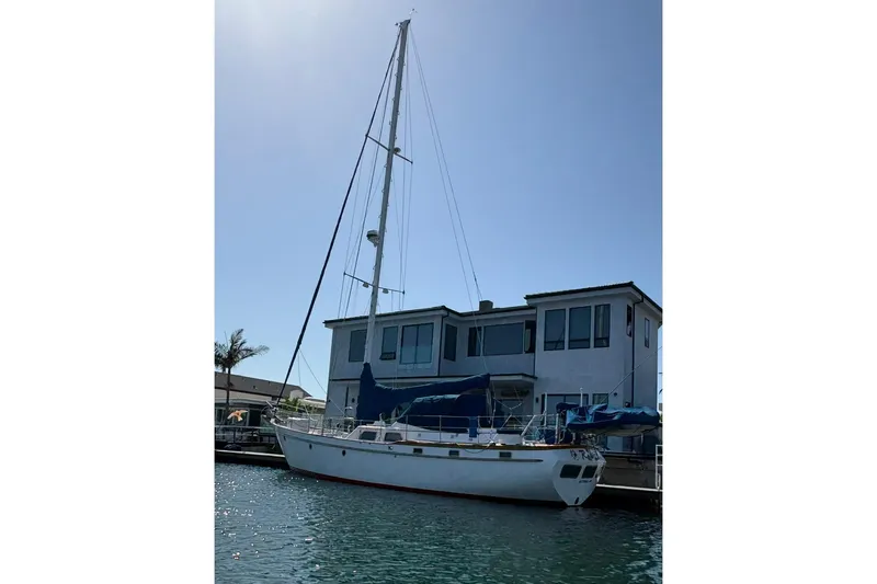1984 Transpacific Marine Ketch docked near a waterfront house under clear skies.