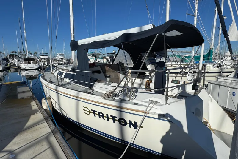 1989 Catalina 42 sailboat named Triton docked at a marina under clear blue skies.