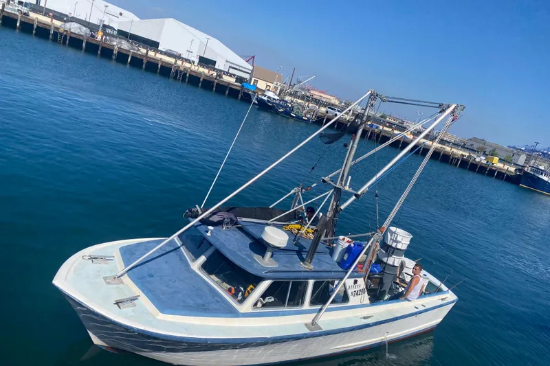 Small fishing boat, Roberts 30 model, 1977, docked in a harbor under clear blue sky.