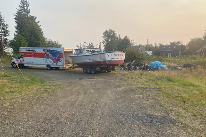 U-Haul truck towing 1977 Roberts 30 boat "Viking Queen" on rural road.