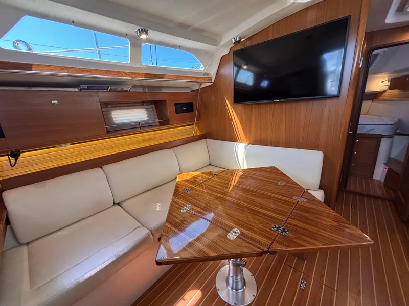 Interior of 2019 Catalina 385 sailboat with wooden table, white seating, and mounted TV.