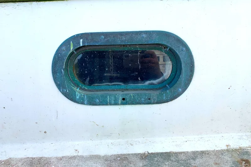 Porthole of 1980 Tayana Pilot House boat with weathered green frame.