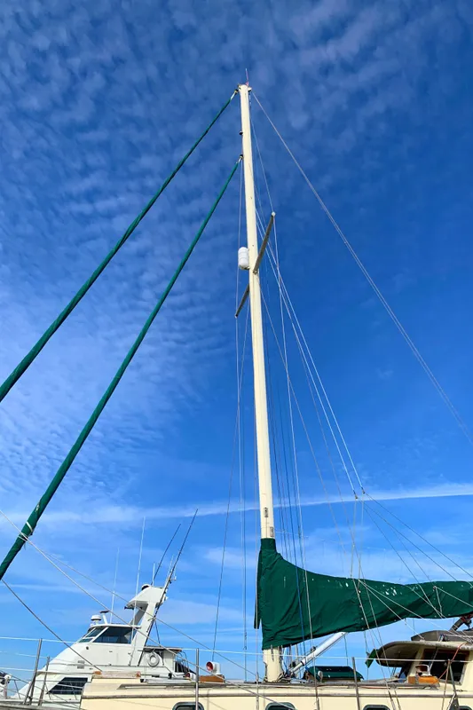 1980 Tayana Pilot House sailboat with tall mast against a clear blue sky.