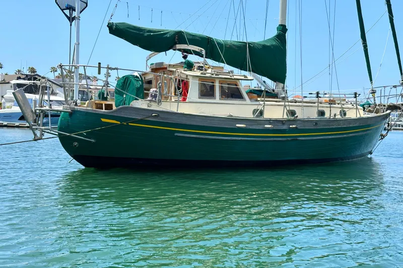 1980 Tayana Pilot House sailboat with green hull and sails docked in marina.