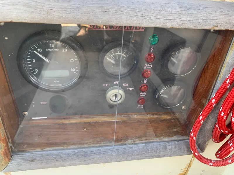 Control panel of a 1980 Tayana Pilot House boat with gauges and red rope.