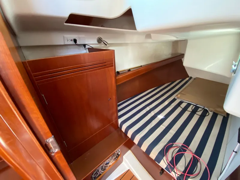 Beneteau 36.7 2004 interior cabin with striped bedding and wooden cabinetry.