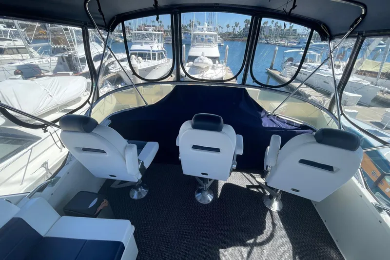 1975 Uniflite Sport Fisher 42 cockpit with three white captain chairs, marina view.