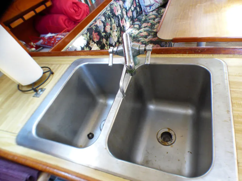 Double sink in 1982 Catalina 38 yacht kitchen with floral seating and wooden table.