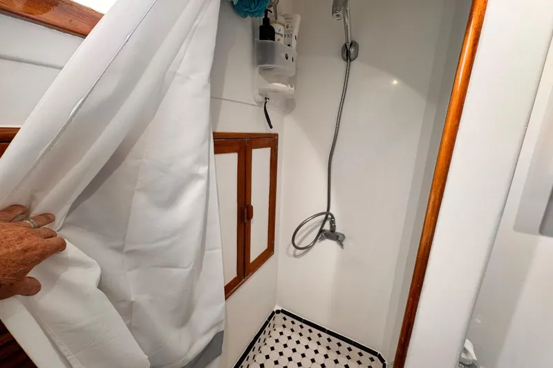 1978 Roughwater 41 boat shower with white curtain and wooden accents.