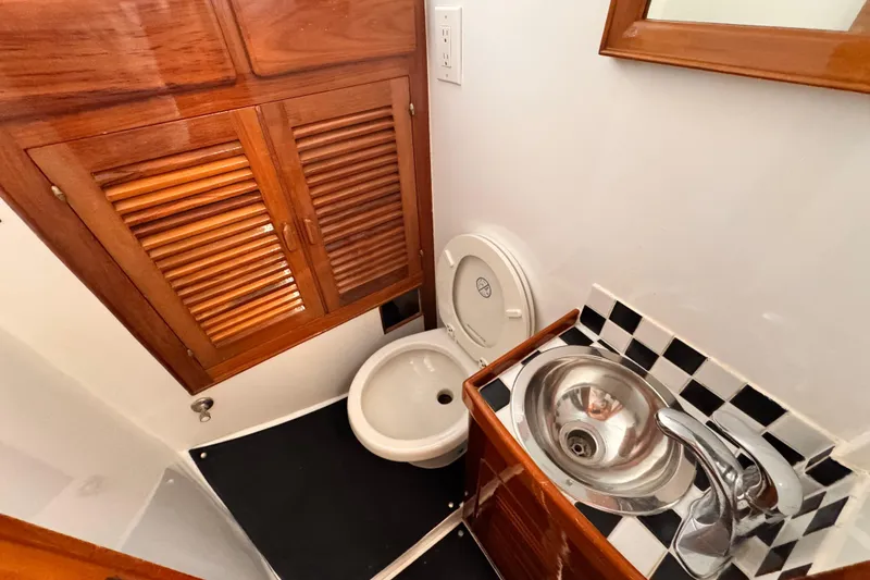 1978 Roughwater 41 boat bathroom with wooden cabinets, toilet, and stainless steel sink.