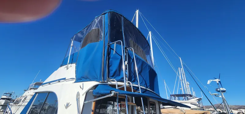 1985 Bertram 33 Flybridge Cruiser with blue canopy, docked under clear blue sky.