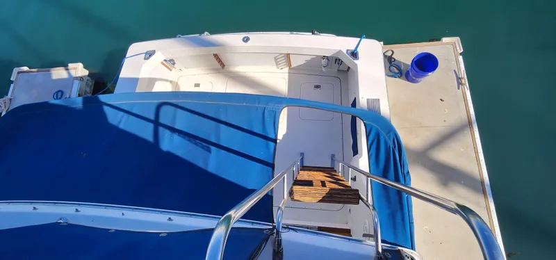 1985 Bertram 33 Flybridge Cruiser docked, view from above, blue cover, wooden steps.