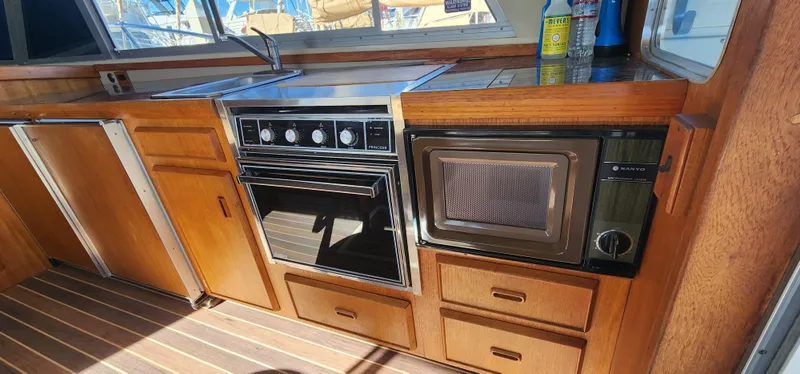 1985 Bertram 33 Flybridge Cruiser kitchen with stove, microwave, and wooden cabinetry.