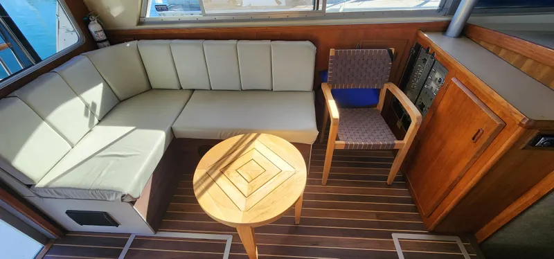 1985 Bertram 33 Flybridge Cruiser interior with beige seating, wooden table, and chair.