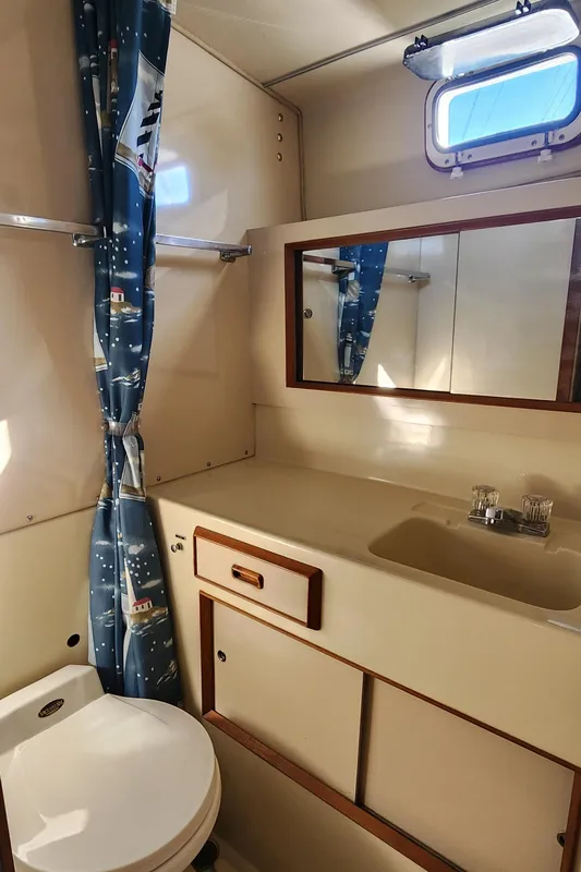 1985 Bertram 33 Flybridge Cruiser bathroom with sink, mirror, and nautical-themed curtain.