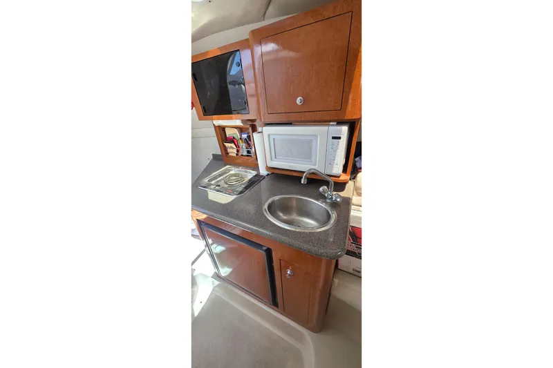 Compact kitchen area in a 2001 Doral 250se boat with sink, microwave, and stove.