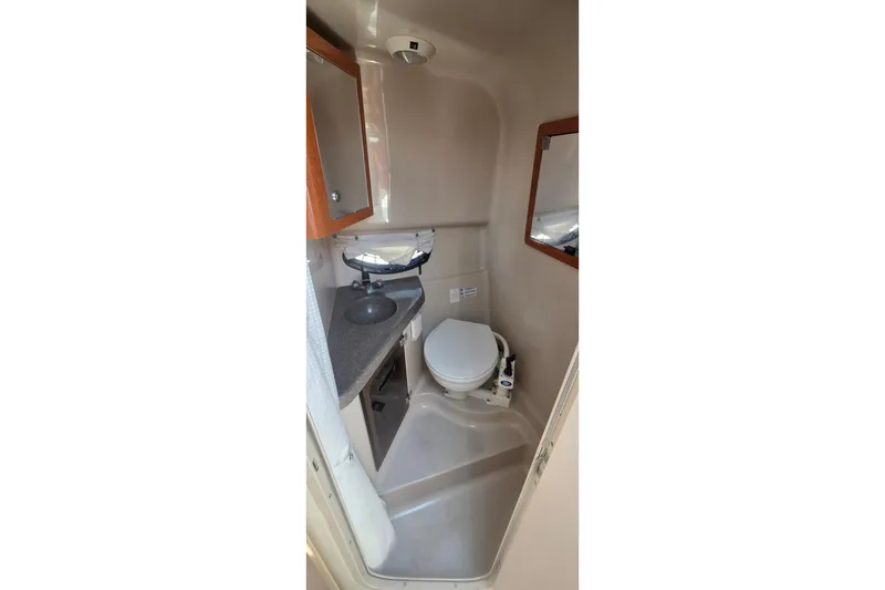 Compact bathroom in a 2001 Doral 250se boat, featuring a toilet, sink, and mirror.