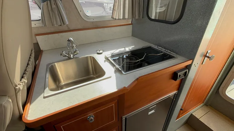 2023 KingFisher 3025 Destination boat kitchen with sink, stove, and compact fridge.