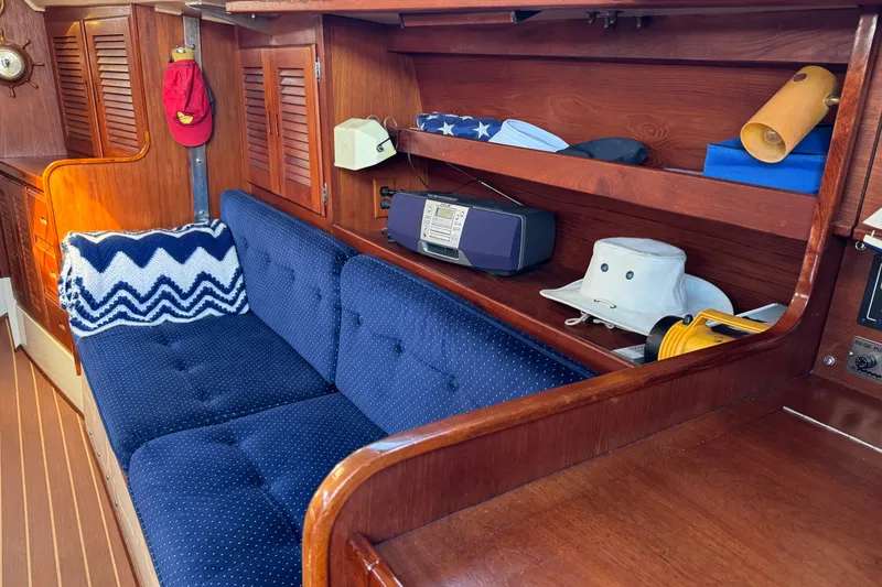 Interior of 1985 Catalina 38 sailboat with blue cushioned seating and wooden shelves.